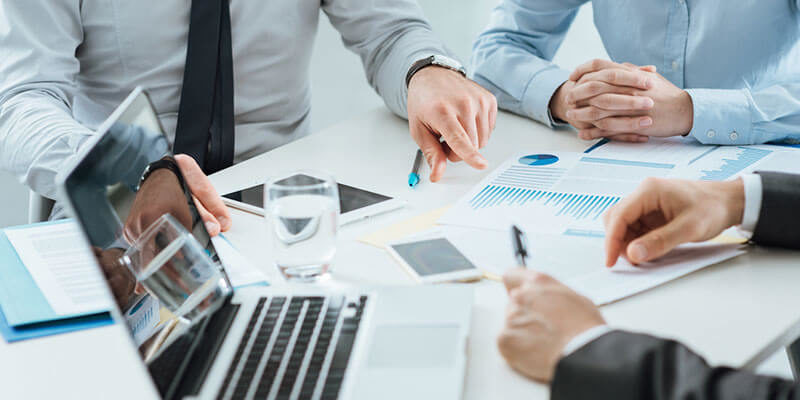 several business professionals look over spreadsheets and laptop documents