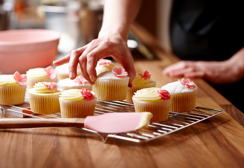 A baker decorating freshly baked cupcakes.