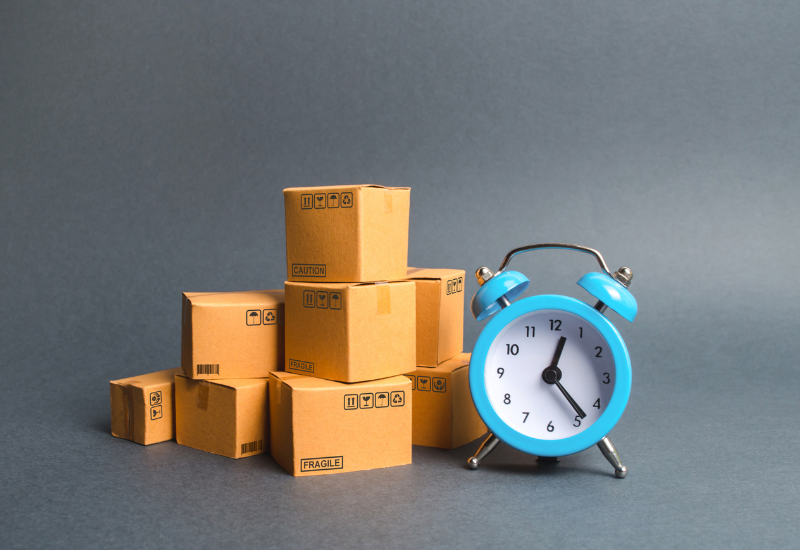 An alarm clock sitting next to multiple sealed boxes.